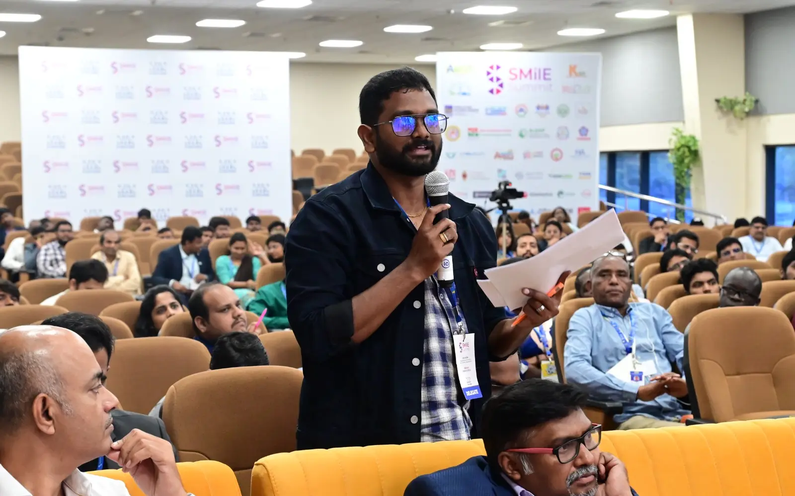 A participant asks a question during a SMilE Summit session in an occupied auditorium